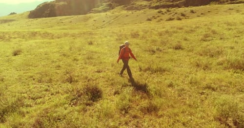 Flight Over Backpack Hiking Tourist Walking Across Green Mountain Field. Huge Rural Valley at Summer