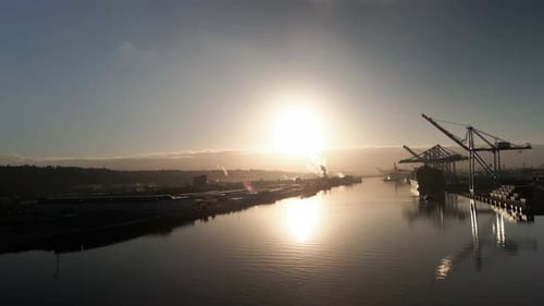 Goldenes Sonnenlicht, das von ruhigem Wasser reflektiert wird, riesige Kräne entladen Container von Schiffen, Antenne