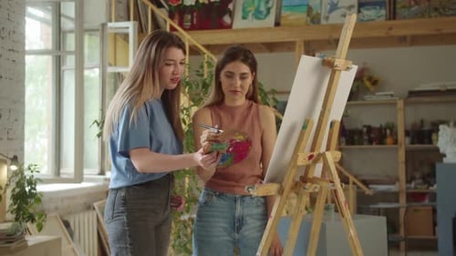 Two Lovely Girlfriends are Standing in the Studio Smiling and Drawing a Picture Together