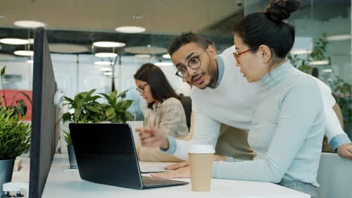 Colleagues Talking Looking at Laptop Screen Working with Computer in Shared Office