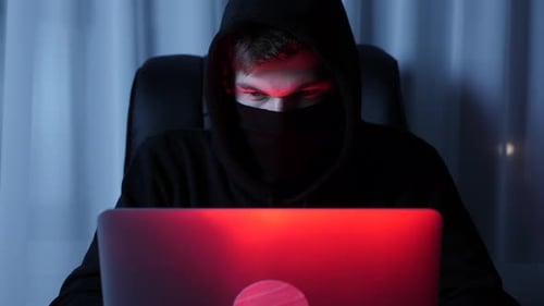 Close up of male hacker looking at laptop screen sitting in dark room
