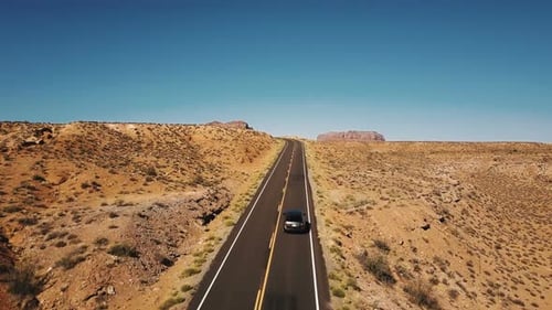 Drone Rising Up Above Car Moving Along Empty Desert Road To Reveal Amazing Mountain Skyline