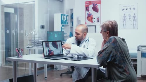 Doctor and Senior Woman Review Heart on Laptop