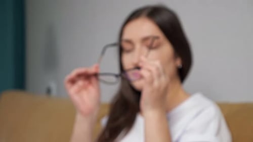 Woman Putting on Glasses Smiling on Sofa