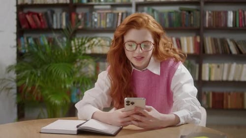 Attractive Student Woman Holding Modern Smartphone Texting Message in Home Office or Library