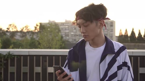 Young Attractive Asian Man Walking Down the Street and Using a Smartphone