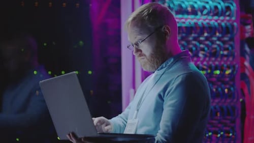 Man Working on Laptop in Dark Server Room