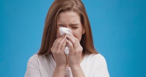 Studio Portrait of Young Sick Lady Blowing Her Nose Blue Background Slow Motion
