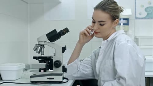 Young Woman Leans on Microscope in Bright Lab