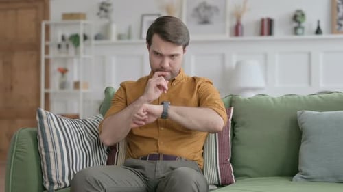 Man Using Smartwatch on Green Couch Indoors