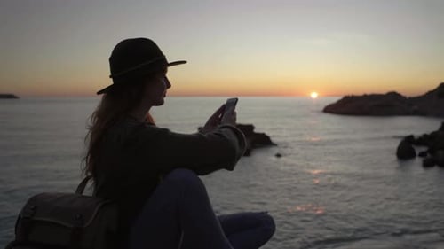 Woman Uses Phone on Cliff During Sunset