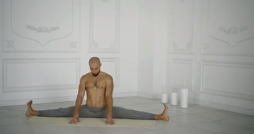 Männlicher Yogi sitzt in geteilter Position in der Halle und meditiert mit geschlossenen Augen