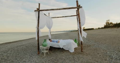 Young girl sleeps in a canopy bed at sunset on the beach near the ocean