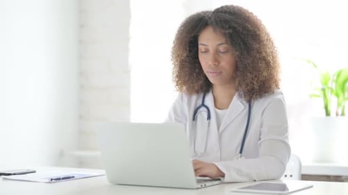 Afrcian Doctor Smiling at Camera while using Laptop in Clinic