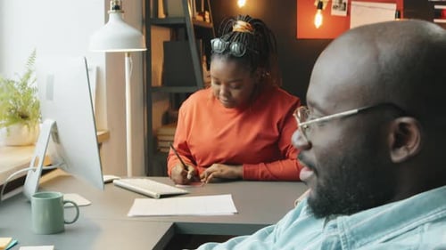 African American Man Using Laptop and Talking with Colleague during Workday