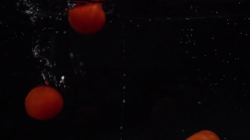 Red Tomatoes Fall and Float in Water. Black Background. Slow Motion. Food Video Tomatoes