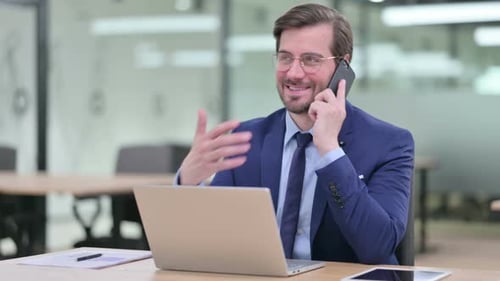 Man in Suit Talks on Phone at Desk