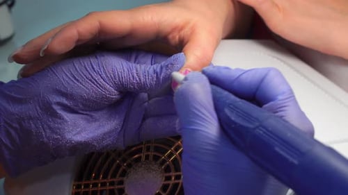Manicure master in blue gloves removes gel polish from nails using a cutter.