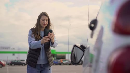 Woman Photographing Car with Smartphone in Parking Lot