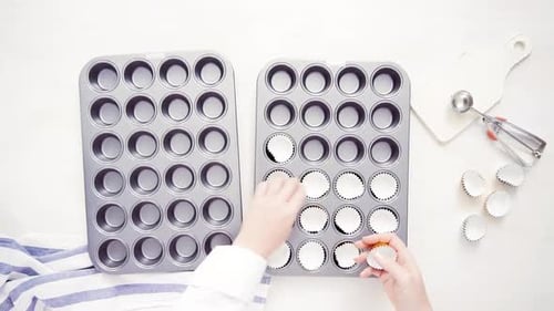 Time lapse. Flat lay. Lining cupcake pan with paper cupcake liners.