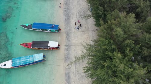 aerial top down of boats anchored on a white sand beach in beautiful turquoise water in Gili Trawang