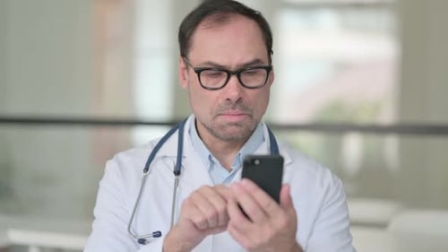 Adult Male Doctor Uses Smartphone in Hospital