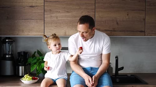 Dad and Daughter Eat Strawberries in Kitchen