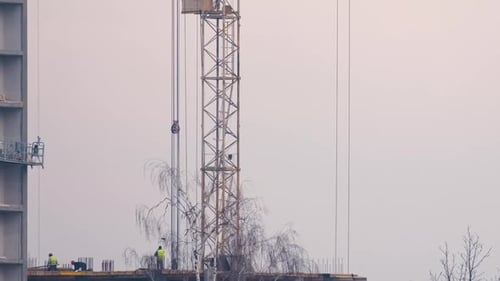Dark Silhouette of Tower Crane and Small Silhouettes of Workers at High Residential Apartment