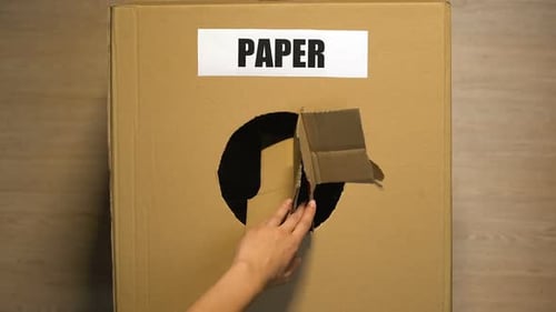 Hand Throws Cardboard into Paper Recycling Bin