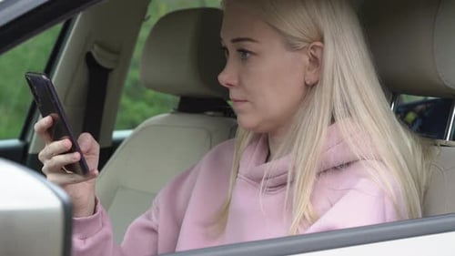Young woman sitting in a car and using smartphone.