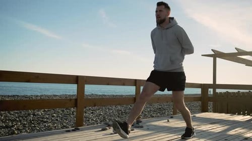 Junger Mann spannt die Beinmuskeln an und macht bei Sonnenaufgang im Freien Kniebeugen