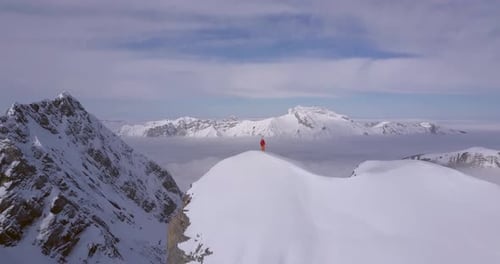 Aerial drone view of a mountain climber skier on the peak summit top of a snow covered mountain