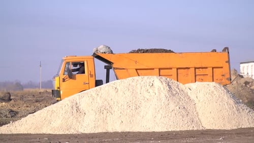 Orange Dump Truck Next to Large Sand Pile
