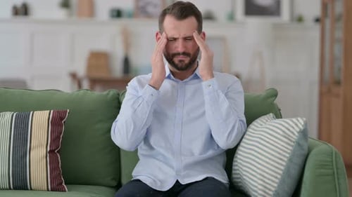Man Sitting on Couch Massaging Temples with Headache