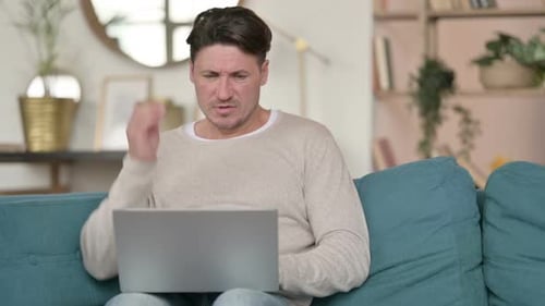 Man Working on Laptop, Massaging Neck at Home