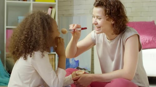 Female Teacher Laughing and Doing Makeup for Little African Girl in Kindergarten