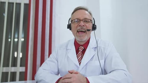 Happy doctor looking at camera. Doctor man sitting at the desk at his working place and smiling at c