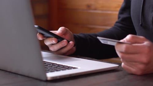 Geschäftsmann in einem schwarzen Hoodie macht Online-Zahlung mit Kreditkarte und Smartphone, Online-Shopping