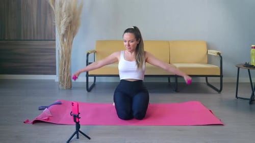 Entrenamiento en casa con mancuernas Una mujer está levantando pesas y viendo un vídeo tutorial en su smartphone
