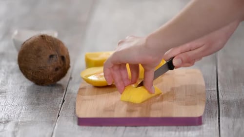 Hands Dice Bright Yellow Mango on Cutting Board