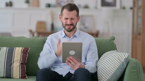 Man Frustrated Using a Tablet on Sofa
