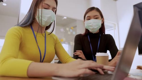 Young people with face masks back at work in office after lockdown.