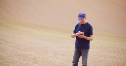 Farmer Examining Agricultural Field While Working on Digital Tablet Computer at Farm.