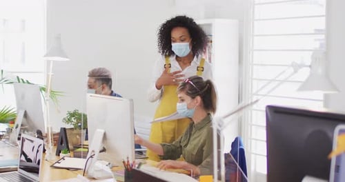 Office colleagues wearing face masks discussing over computer at office