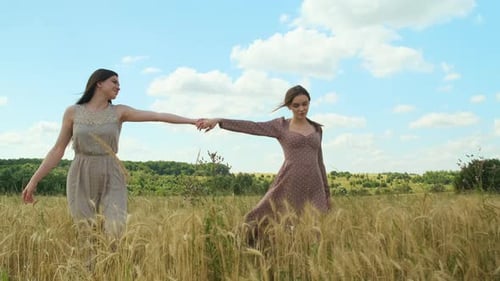 Two Enchanting LGBT Women Walking Holding Hands in Wheat Field in Beautiful Dresses and Looking at