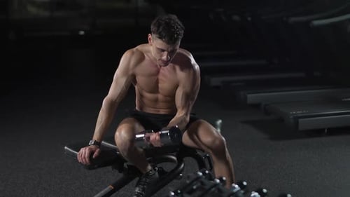 Un hombre atlético entrena en el gimnasio, levanta mancuernas y realiza ejercicios con las manos, un atleta ejercita su