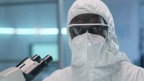 Scientist in Protective Suit Next to Microscope