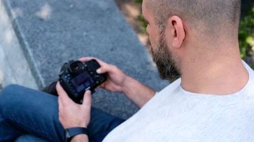 Man Sits Outdoors With Camera in Urban Setting