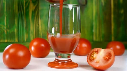 Frischer Tomatensaft in ein leeres transparentes Glas gegossen, neben frischen reifen natürlichen Tomaten