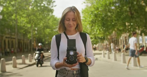 Woman Adjusting Vintage Camera on Sunny City Street